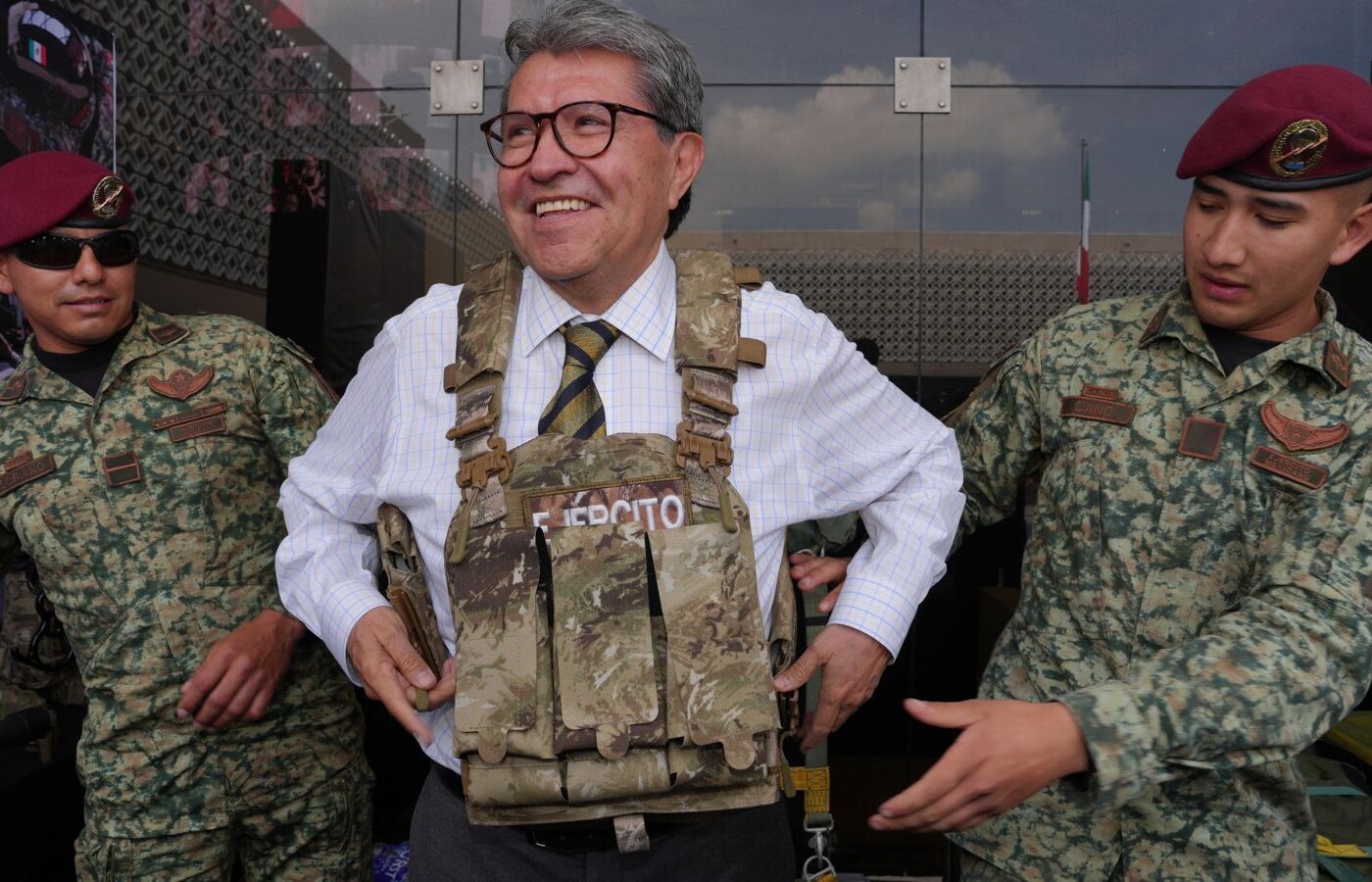 Ricardo Monreal prueba un chaleco táctico acompañado de dos militares durante una exhibición.